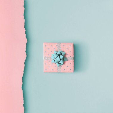 Pembe ve mavi arka planda mavi kurdeleyle sarılı küçük bir hediye kutusundan yapılmış Noel minimalist kompozisyonu. Noel arkaplanı. Minimum konsept. Düz yatıyordu. Yukarıdan. Yazmak için boşluk