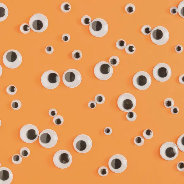 Halloween monster eyes orange background. Funny holiday flat lay concept.