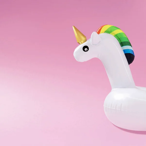 Creative art minimal aesthetic. Inflatable unicorn pool toy on pastel pink background. Minimal summer concept