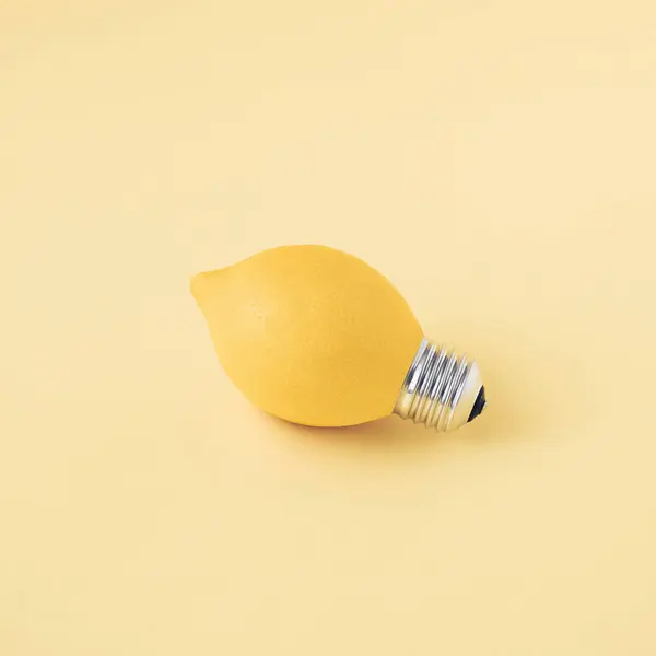 A single fresh lemon as a light bulb isolated on a bright yellow background. Trendy fruit idea. Abstract and surreal healthy diet. Creative food concept.