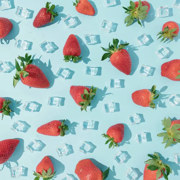 Summer fruit  pattern made with fresh strawberries and ice cubes on vibrant blue background. Creative fruit  texture concept.  Minimal top down fruit concept.