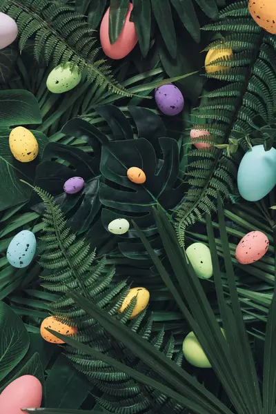 Creative Easter nature background.Green tropical palm leaves with Easter eggs.Minimal spring abstract jungle or forest composition.Contemporary style Holiday Easter celebration greeting card or idea.