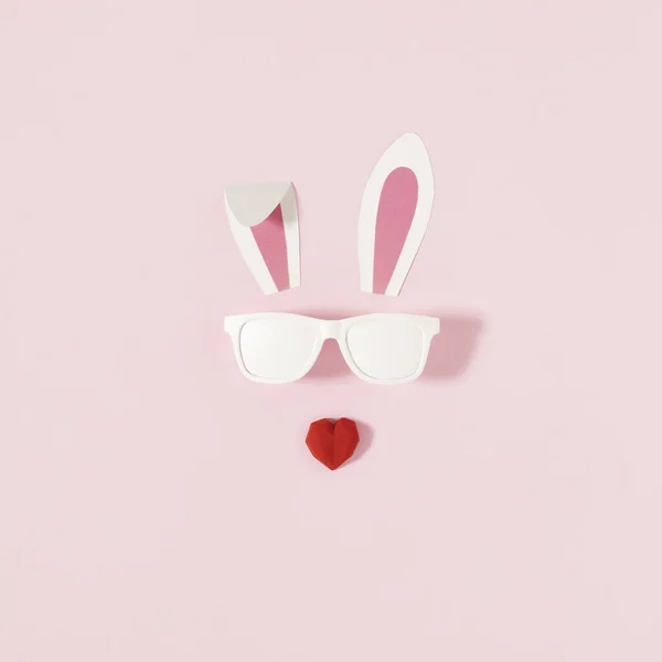 Bunny rabbit face made of rabbit ears with sunglasses on bright pink background,with a red heart-shaped snout.Creative  minimal Easter holiday concept.Holiday Easter celebration greeting card or idea