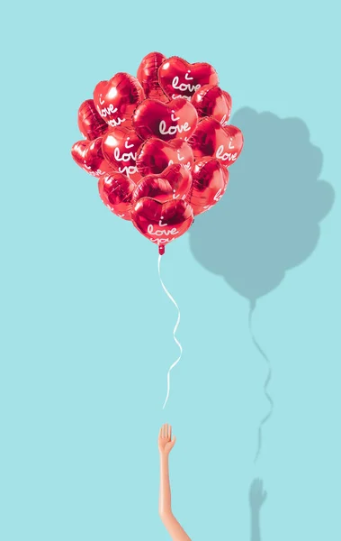 Creative composition made with Bunch of red color heart shaped foil balloons and doll hand on pastel blue background. Minimal concept of Valentine\'s Day or love. Creative art, minimal aesthetics.