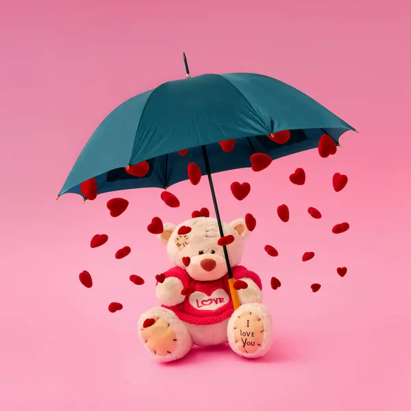 Love composition made of teddy bear, umbrella and rain in the shape of a heart on pastel pink background. Minimal concept of Valentine\'s Day or love. Creative art, minimal aesthetics.