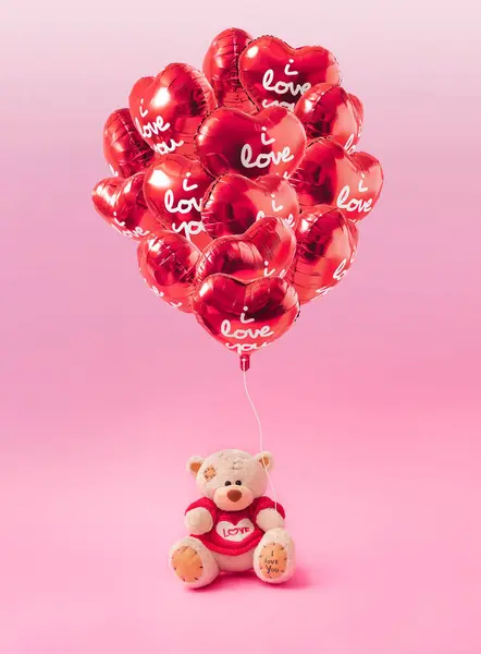 Love composition made of teddy bear and Bunch of red color heart shaped foil balloons on pastel pink background. Minimal concept of Valentine\'s Day or love. Creative art, minimal aesthetics.