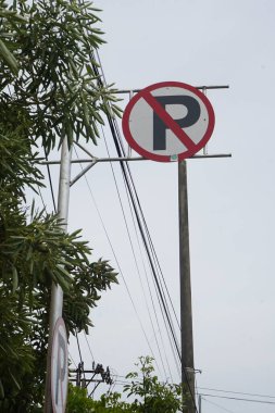 no parking sign on the side of the road with trees and electricity poles in the background