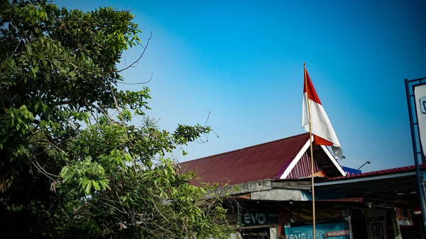 背景がインドネシアの独立記念日を歓迎する明確な空に対してポールの上に赤と白の旗 — ストック写真