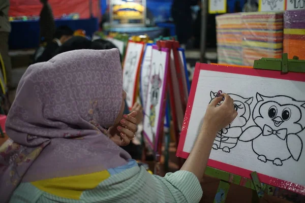 a young woman is coloring a picture on a white canvas at a night market stall