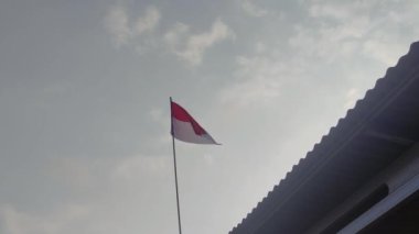 Kırmızı ve beyaz bayrağın 4k videosu, Endonezya ulusal bayrağı açık bir gökyüzünün arka planında gün boyunca dalgalanıyor.