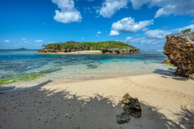 Okinawa 'daki Motobu Bölgesi, Bise Plajı' nın berrak suları. Mercan çıkıntılı beyaz kumsal ve açık denizde küçük adalar.