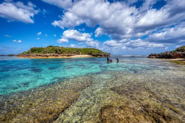 Okinawa 'daki Motobu Bölgesi, Bise Plajı' nın berrak suları. Mercan çıkıntılı beyaz kumsal ve açık denizde küçük adalar.