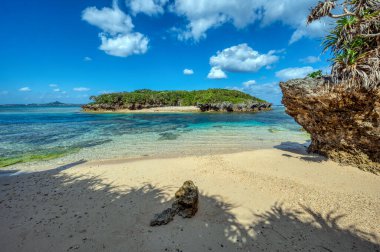Okinawa 'daki Motobu Bölgesi, Bise Plajı' nın berrak suları. Mercan çıkıntılı beyaz kumsal ve açık denizde küçük adalar.