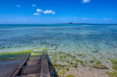 Okinawa 'daki Motobu Bölgesi, Bise Plajı' nın berrak suları. Mercan çıkıntılı beyaz kumsal ve açık denizde küçük adalar.