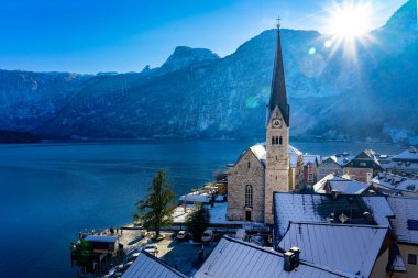 beautiful sunny cityscape of the special city Hallstatt in Austria Salzkammergut snowy winter mountains and lake and church . clipart