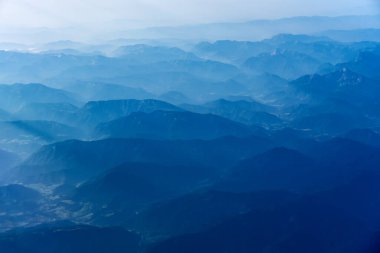 Alplerin üzerinden uçan uçağın sisli zirveleri. .