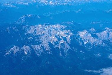 Alplerin üzerinden uçan uçağın sisli zirveleri. .