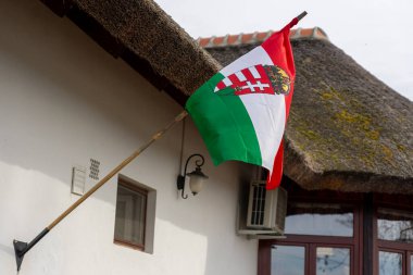 Geleneksel saman çatı evine yerleştirilmiş armalı Macar bayrağı .