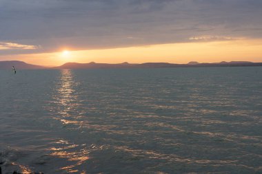 Balaton Gölü üzerinde rüzgar sörfü yapan bir kadınla güzel bir gün batımı. .