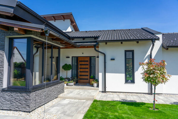 A contemporary house entrance showcasing sleek architecture, greenery, and a welcoming pathway, emphasizing modern design elements and harmonious outdoor integration.