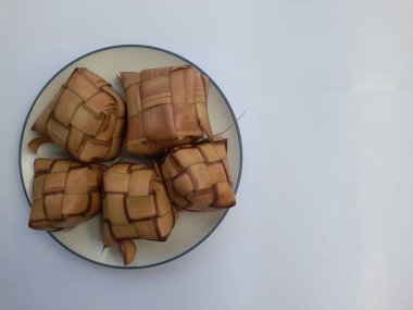 Hindistan cevizi yapraklarına sarılı ketupat yiyeceği beyaz arka planda bir tabakta. Sağlıklı gıda geçmişi, yemek tarifi, pirinç, kahvaltı, öğle yemeği, akşam yemeği, yemek, yemek, yemek, yemek, yemek, yemek