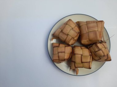 Hindistan cevizi yapraklarına sarılı ketupat yiyeceği beyaz arka planda bir tabakta. Sağlıklı gıda geçmişi, yemek tarifi, pirinç, kahvaltı, öğle yemeği, akşam yemeği, yemek, yemek, yemek, yemek, yemek, yemek