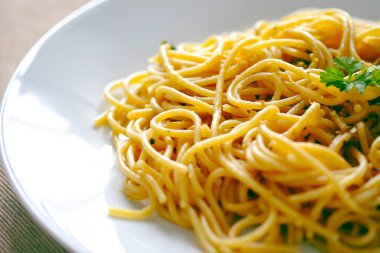 Beyaz tabakta sebzeli spagetti, yeşil peçetede servis edilen İtalyan yemeği.. 