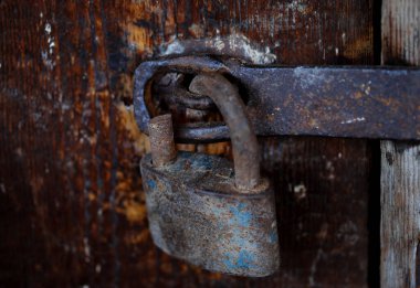 Eski paslı bir asma kilidin, yıpranmış ahşap bir kapının üzerinde, yaşı, çürümeyi ve güvenliği sembolize ediyor..