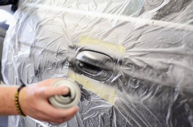 Tamirat sırasında maskeli arabanın kapı koluna boya sıkan tamirci, atölyeye sprey kutusuyla el sıkıp yeni bir ceket takan tamirci..