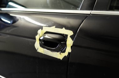 Yeni boyanmış siyah araba kapı kolu, etrafta maske bandı, araç tamiri ve otomobil atölyesinde bitirme işlemleri..