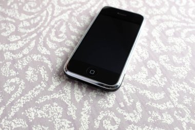 Zbrasav, Czech Republic - April 8, 2018: Editorial photograph of the first generation Apple iPhone 2G on light gray damask textile with floral pattern. Editorial use only.