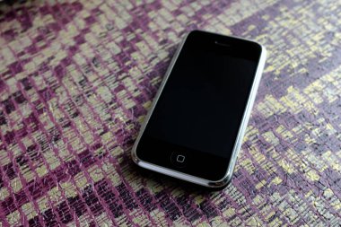 Zbrasav, Czech Republic - April 8, 2018: Editorial photograph of the first generation Apple iPhone 2G on purple and yellow woven fabric background. Editorial use only.