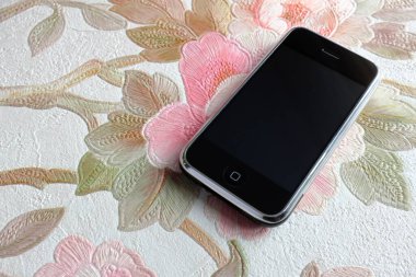 Zbrasav, Czech Republic - April 8, 2018: Editorial photograph of the first generation Apple iPhone 2G on pink rose floral fabric background. Editorial use only.