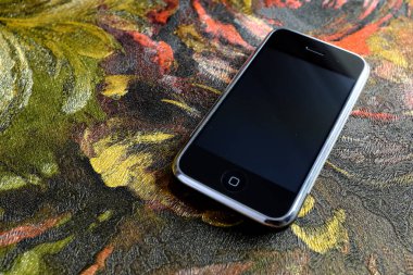 Zbrasav, Czech Republic - April 8, 2018: Editorial photograph of the first generation Apple iPhone 2G on dark abstract painted fabric background. Editorial use only.