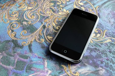 Zbrasav, Czech Republic - April 8, 2018: Editorial photograph of the first generation Apple iPhone 2G on blue ornamental fabric background. Editorial use only.