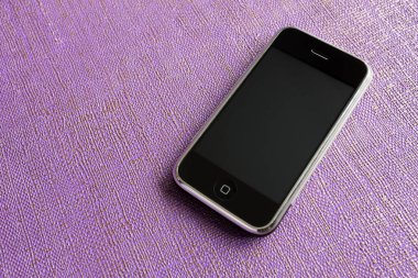 Zbrasav, Czech Republic - April 8, 2018: Editorial photograph of the first generation Apple iPhone 2G on purple textile fabric background. Editorial use only.