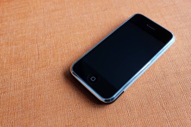 Zbrasav, Czech Republic - April 8, 2018: Editorial photograph of the first generation Apple iPhone 2G on dark orange textured fabric background. Editorial use only.