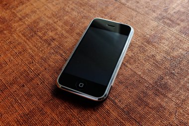 Zbrasav, Czech Republic - April 8, 2018: Editorial photograph of the first generation Apple iPhone 2G on brown wood textured background. Editorial use only.