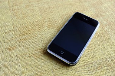 Zbrasav, Czech Republic - April 8, 2018: Editorial photograph of the first generation Apple iPhone 2G on yellow textile fabric background. Editorial use only.