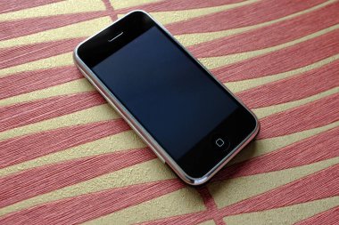 Zbrasav, Czech Republic - April 8, 2018: Editorial photograph of the first generation Apple iPhone 2G on red striped fabric background. Editorial use only.