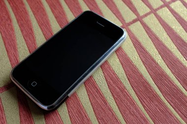 Zbrasav, Czech Republic - April 8, 2018: Editorial photograph of the first generation Apple iPhone 2G on red and orange palm leaf patterned fabric background. Editorial use only.