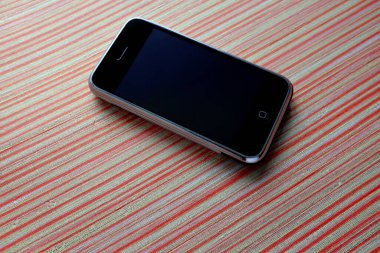 Zbrasav, Czech Republic - April 8, 2018: Editorial photograph of the first generation Apple iPhone 2G on red striped textile fabric background. Editorial use only.