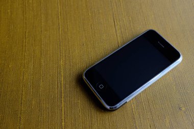 Zbrasav, Czech Republic - April 8, 2018: Editorial photograph of the first generation Apple iPhone 2G on golden textured textile background. Editorial use only.