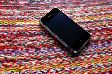 Zbrasav, Czech Republic - April 8, 2018: Editorial photograph of the first generation Apple iPhone 2G on multicolored striped fabric background in red and yellow. Editorial use only.