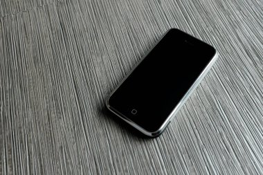 Zbrasav, Czech Republic - April 8, 2018: Editorial photograph of the first generation Apple iPhone 2G on striped fabric background in dark gray tones. Editorial use only.