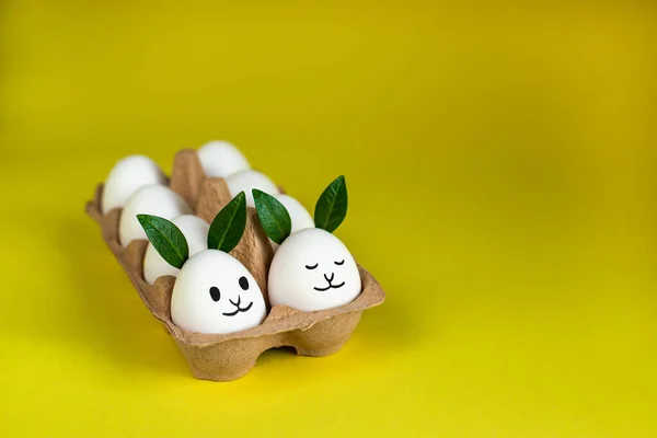 Fancy white Easter eggs with funny green bunny ears in paper tray on yellow background. Traditional spring concept.
