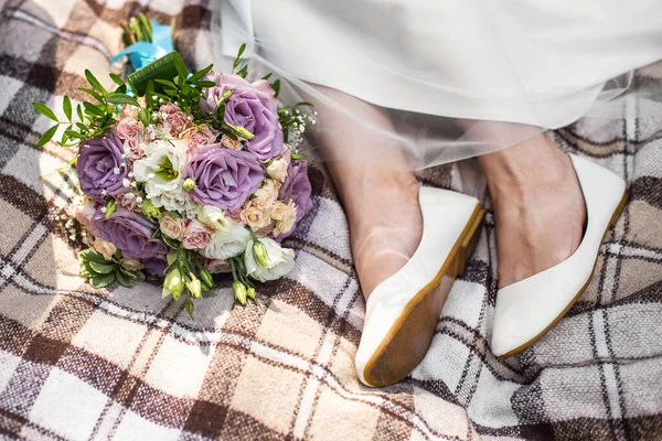 Bride\'s feet and wedding bouquet on brown blanket. Small rustic wedding, micro wedding