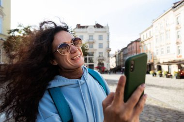 Neşeli, kıvırcık saçlı, güneş gözlüğü takan gezgin kadın...