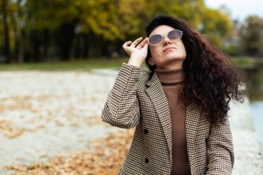 Kıvırcık saçlı, gülümseyen, güneş gözlüklü kadın Park Gölü 'nde dinleniyor.