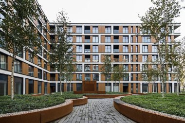 Bir Avrupa şehrinde konut binaları. Modern apartman blokları. Bahçede bitki örtüsü ve ışıklandırma var. Paslı metal kaplama, korten. Yeraltı garajı